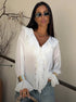 Woman wearing sheer white ruffle blouse with deep V-neck and gold cuff details.