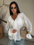 Sheer white blouse with ruffled trim styled with light denim and beige purse.