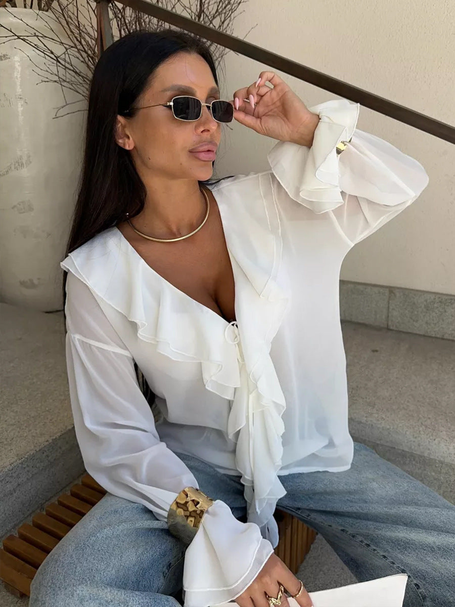 Woman in sheer white blouse with cascading front ruffles and gold statement bracelet.