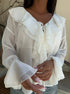 Close-up of sheer white blouse showing neckline tie and layered ruffle cuffs.