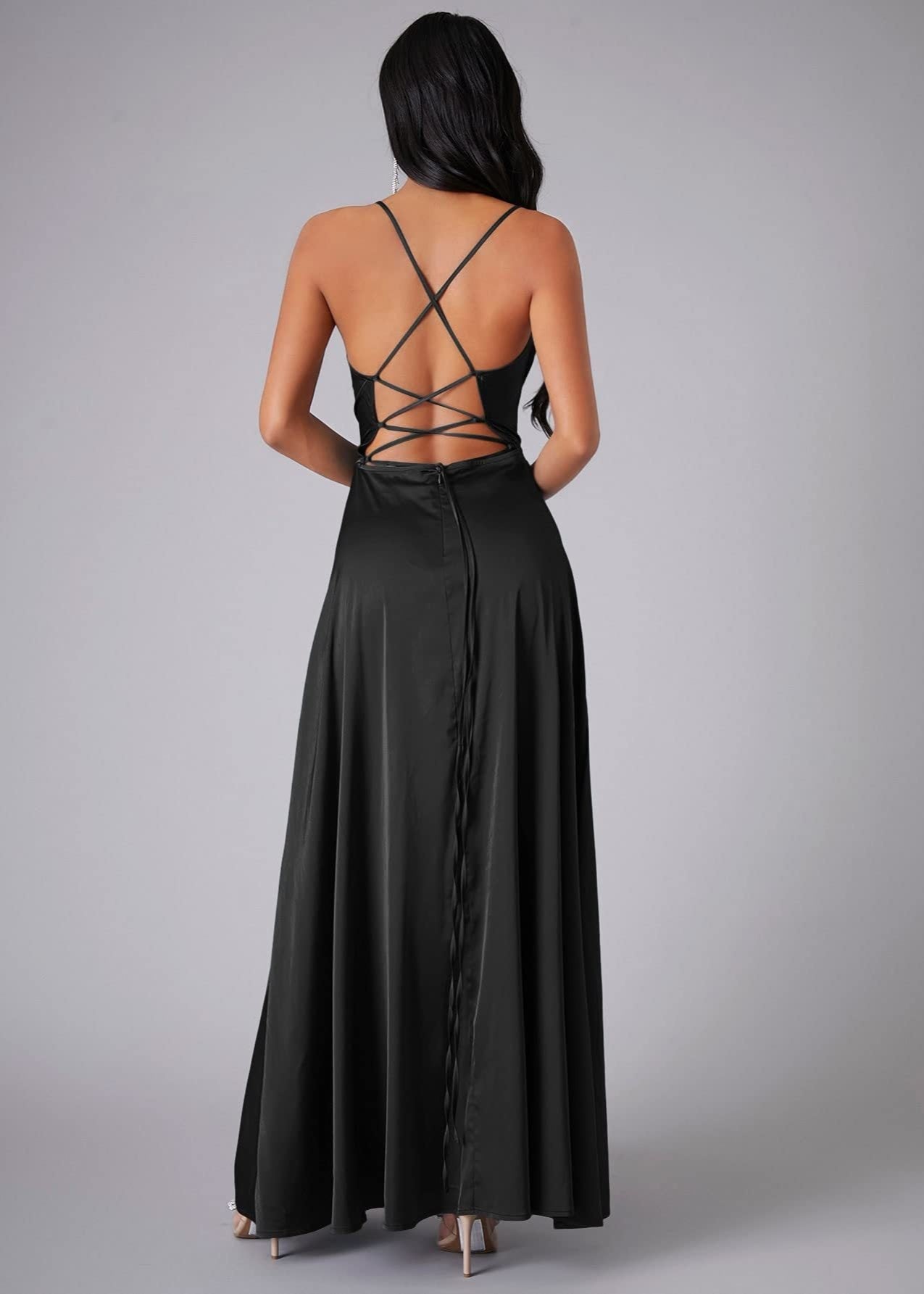 Back view of woman wearing a black dress with criss-cross straps on a gray background