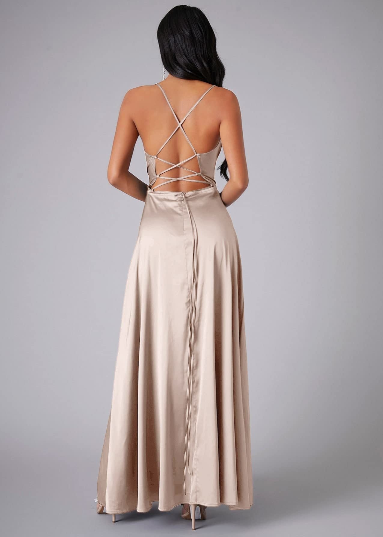 Back of woman wearing a champagne  evening gown with a backless design on a gray background