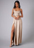 Woman wearing a champagne strapless gown with a high slit on a gray background