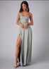 Woman wearing a long, light gray prom dress with a slit on a plain background