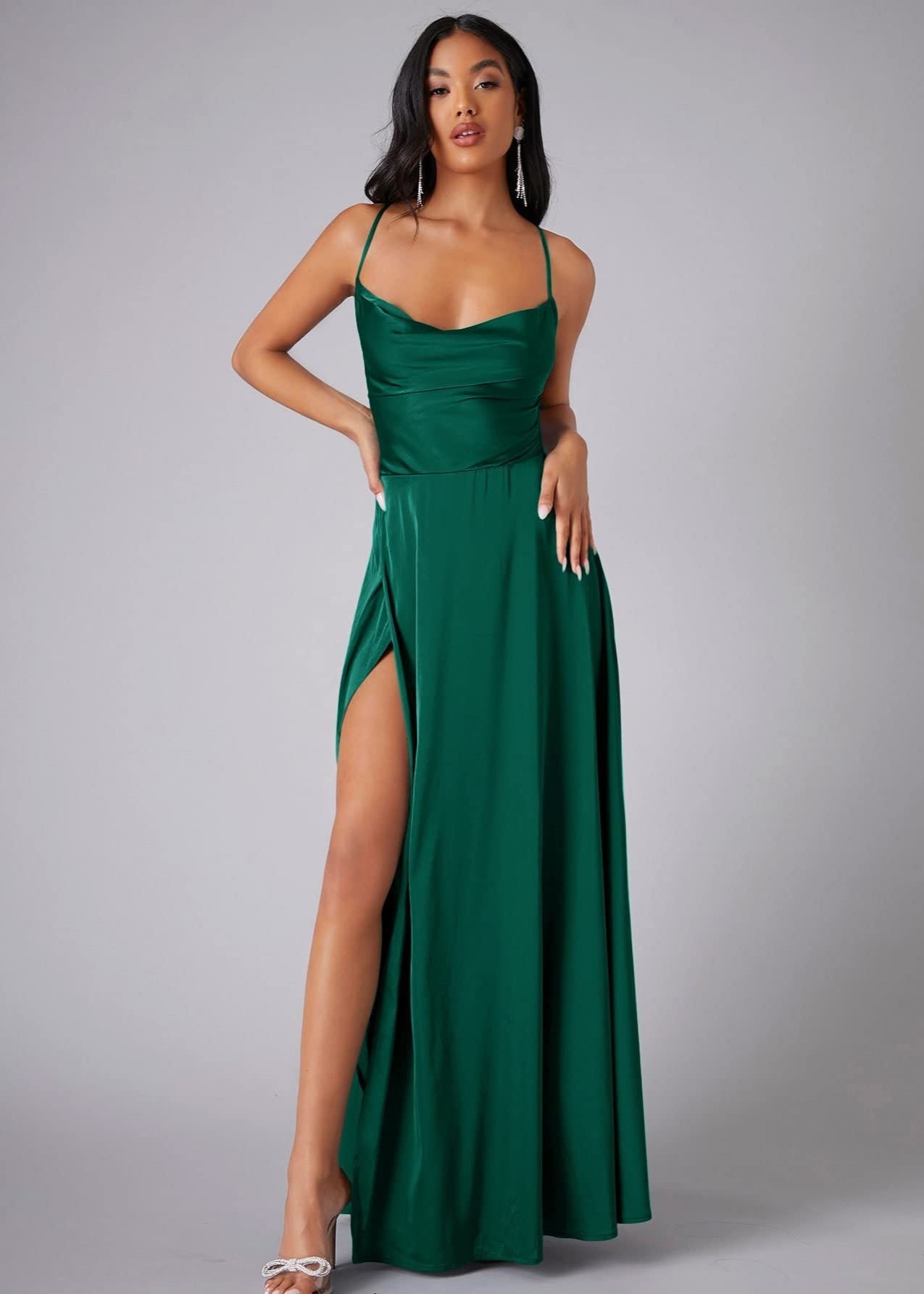 Woman wearing a green evening gown with a high slit on a gray background