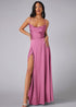 Woman wearing a pink evening gown with a high slit on a gray background