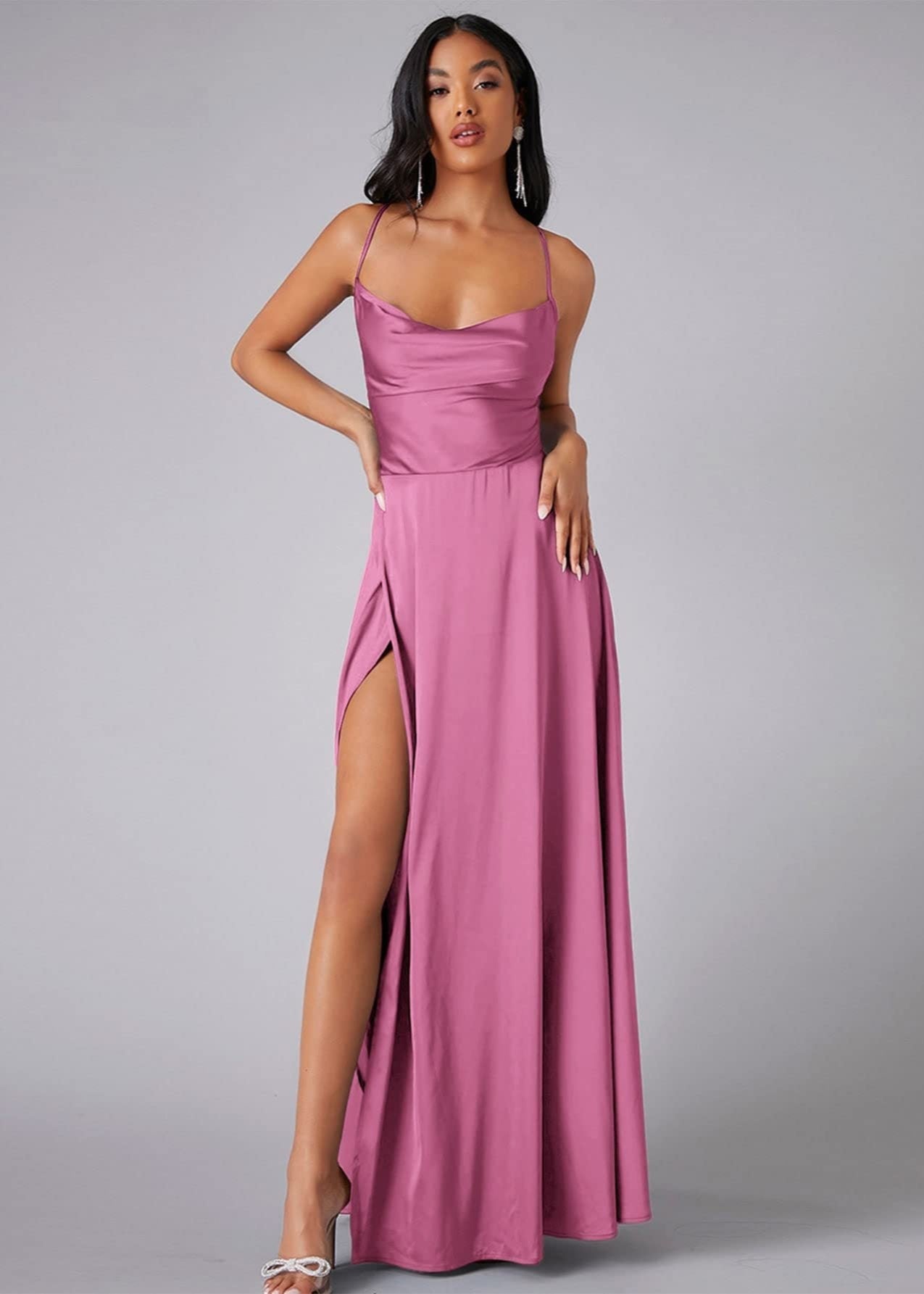 Woman wearing a pink evening gown with a high slit on a gray background