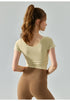 Back view of beige short sleeve yoga top with scoop neckline and snug fit.