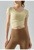 Beige short sleeve yoga top with cropped fit and cross-pleat detail.