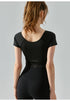Back view of black short sleeve yoga top with sculpting cross-pleat detail and cropped cut.