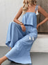 Model sits wearing blue cami top and flowy tiered pants with tassels.