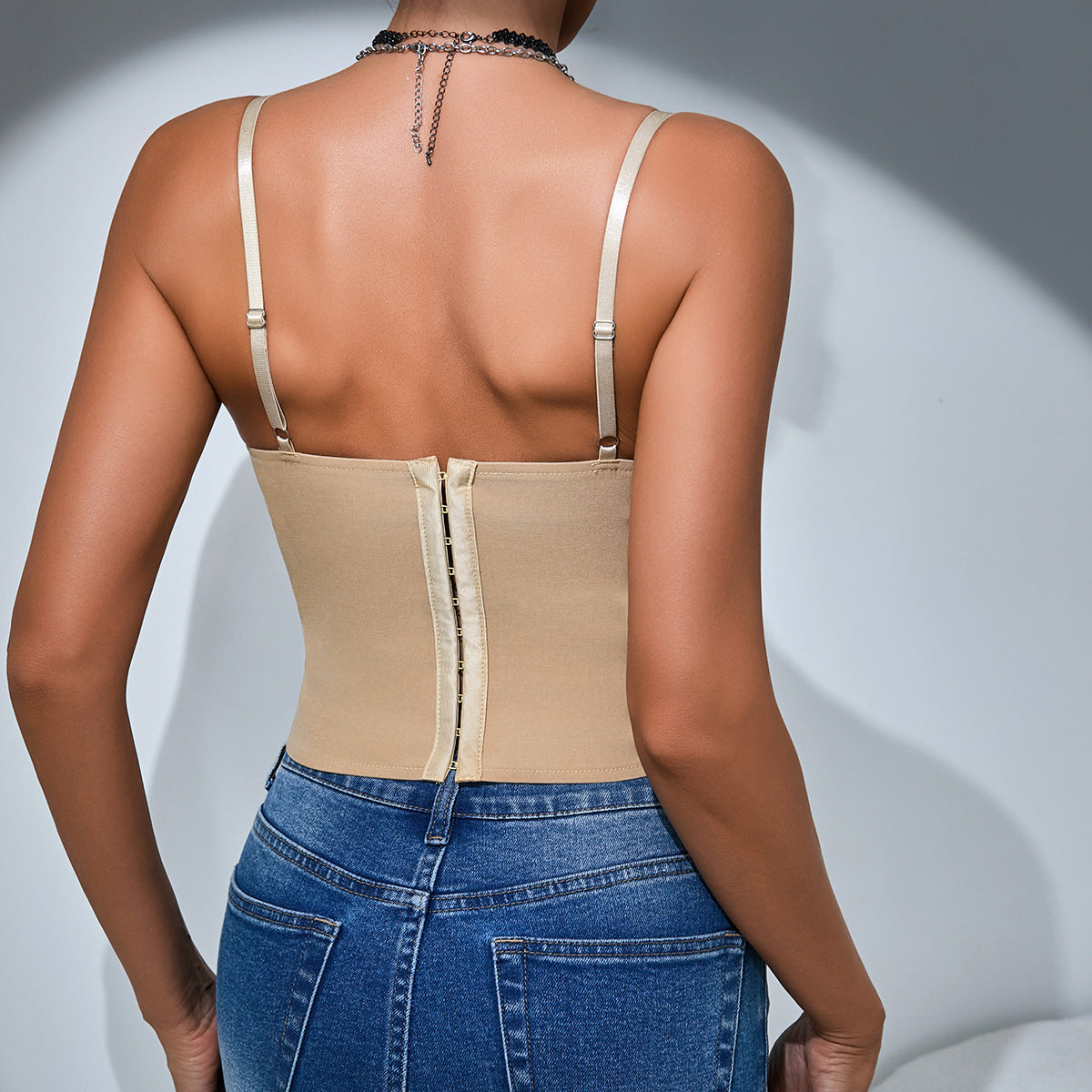 Back view of woman in beige corset top and blue jeans, showing hook-and-eye closure.