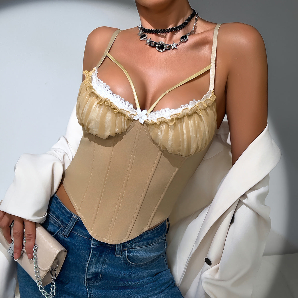Woman in beige corset with lace detail and jeans, draped in white blazer.