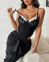 Woman in a black lace-trimmed corset top and ruched skirt pulling at a shoulder strap.