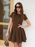 Model in brown fit-and-flare mini dress holding a designer handbag.