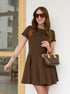 Smiling woman in brown flared mini dress with short sleeves and printed handbag.