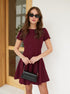 Woman wearing burgundy short sleeve mini dress with flared skirt and black handbag.