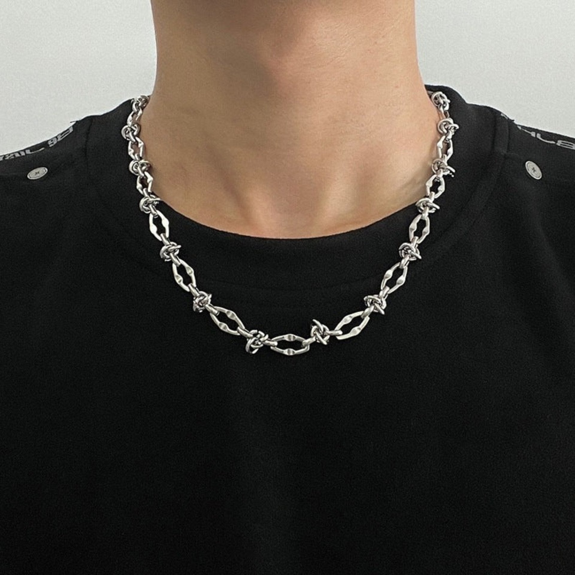 Man wears silver barbed wire necklace with twisted links on black shirt.
