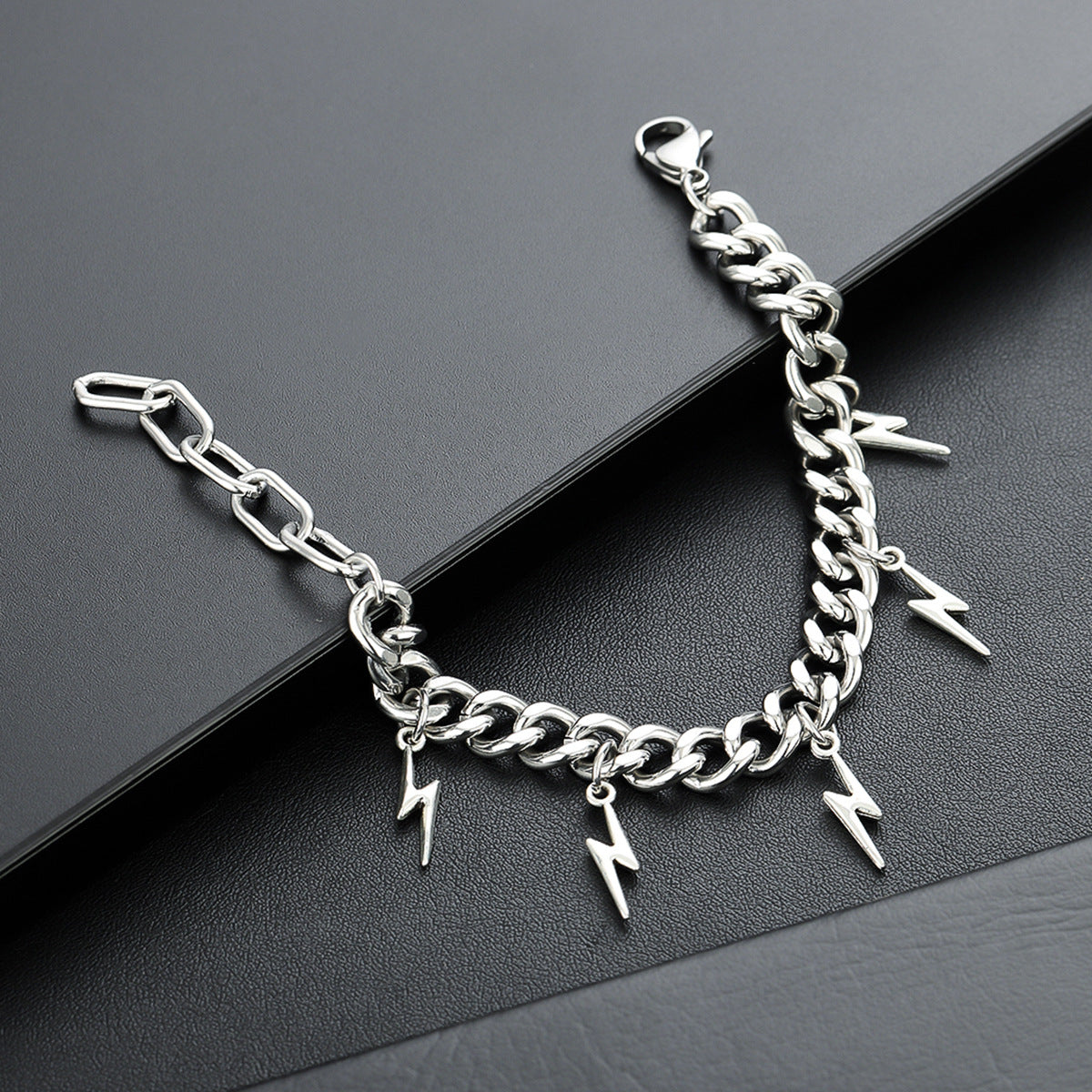 Silver Cuban chain bracelet with lightning bolt charms on black surface.
