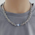 Man wears layered silver chain necklace with blue detail tag.