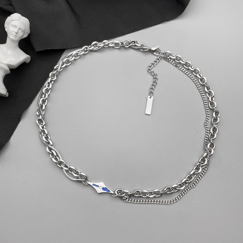 Mixed-link silver chain necklace with blue detail on gray background.