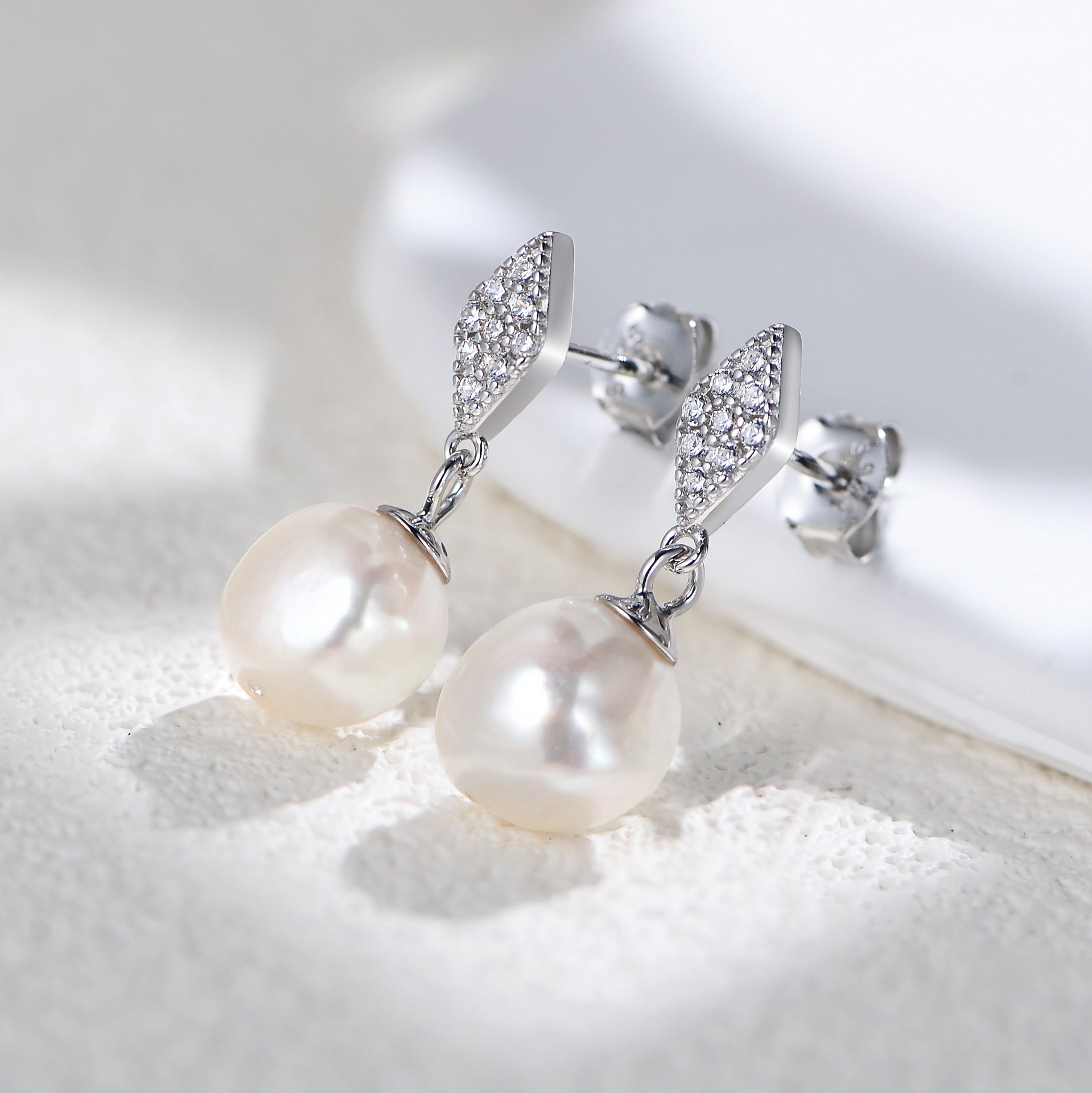 Silver-tone pearl drop earrings, diamond-shaped studs, close-up