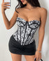 Woman posing against a white wall in a black floral jacquard corset and faux leather mini skirt.