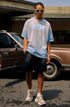 Man wears blue gradient quote tee with black shorts and chunky sneakers, standing in front of a vintage car.