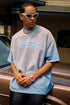 Man leans on vintage car wearing blue quote tee, sunglasses, and silver watch.
