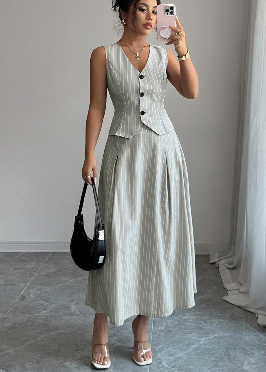 Woman in striped two piece set with sleeveless vest and midi skirt holding black handbag