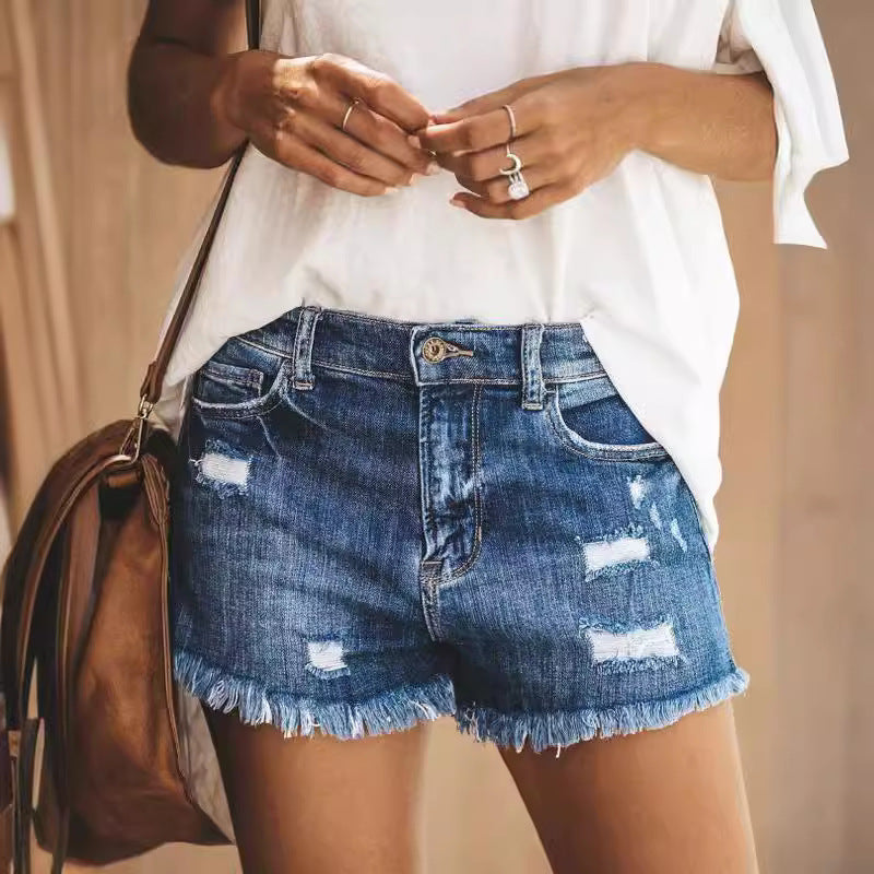 Close-up of woman’s waist wearing dark wash ripped denim shorts and a loose white t-shirt.