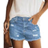 Woman wearing light blue ripped denim shorts with raw hems and a loose white top outdoors.