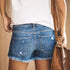  Back view of woman wearing ripped denim shorts with raw hems and carrying a brown shoulder bag.