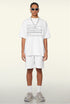 Model wears white crash report tee with white shorts and silver chain.