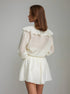 Back of woman wearing a beige 2-piece set with a ruffled collar against a plain background