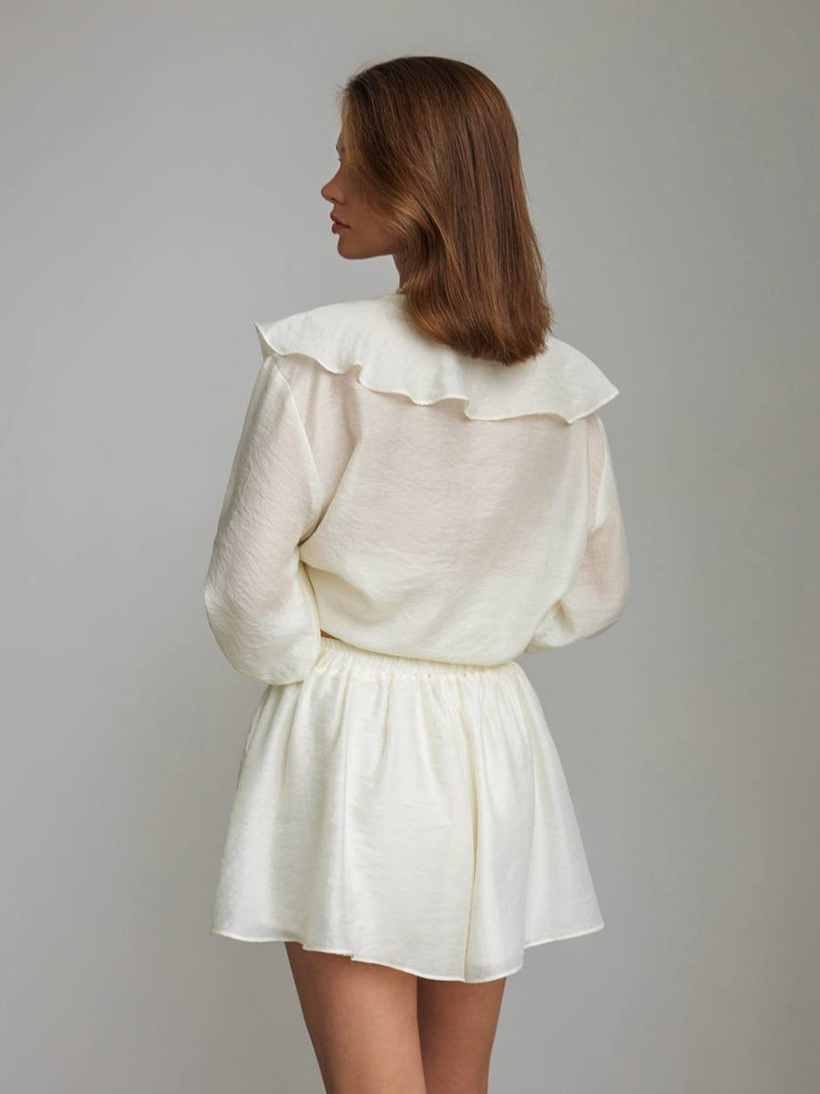 Back of woman wearing a beige 2-piece set with a ruffled collar against a plain background