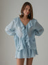 Woman wearing a light blue ruffled blouse set against a gray background
