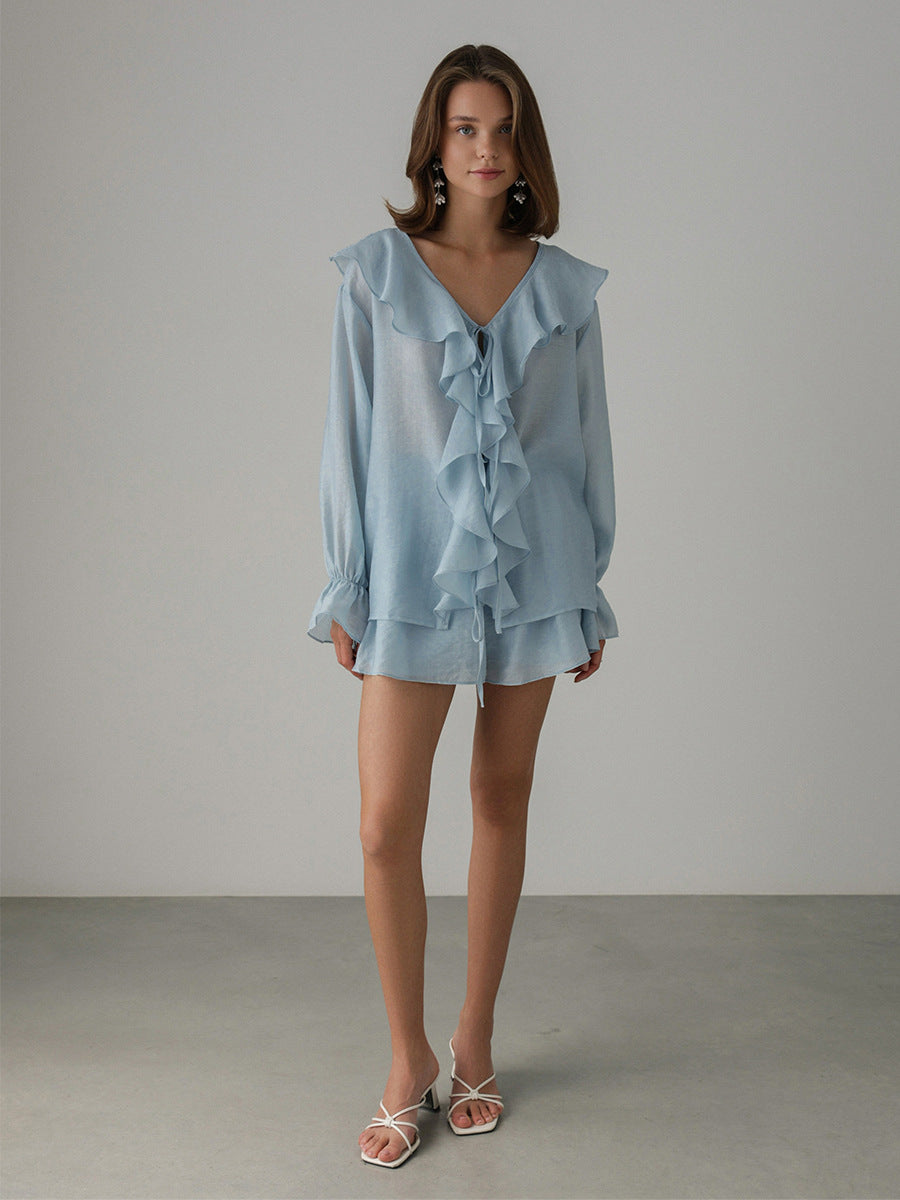 Woman wearing a light blue ruffled blouse and shorts set against a plain background