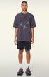 Model in purple "Terrible Beauty" tee with shorts and sneakers.