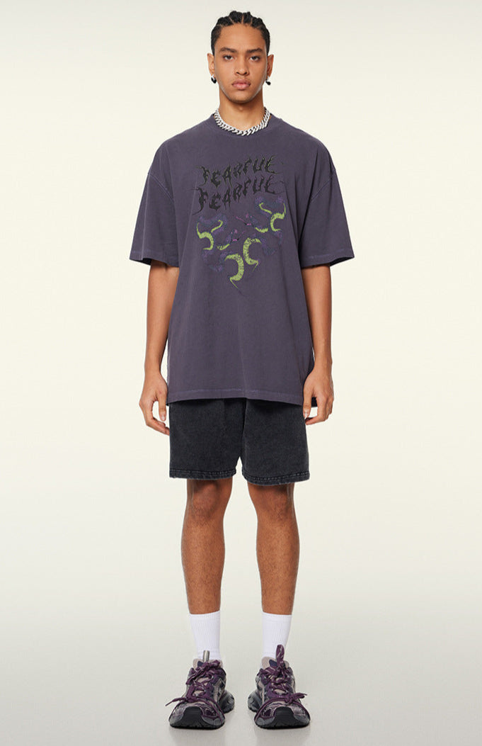 Model in purple "Terrible Beauty" tee with shorts and sneakers.