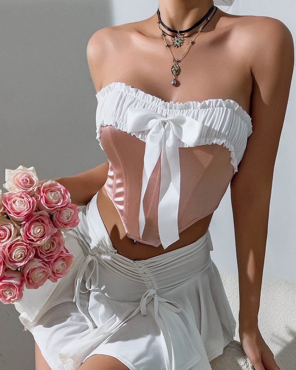 Woman wears blush pink velvet strapless corset with white ruffle trim and front bow, holding bouquet of roses.