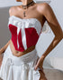 Side view of red velvet strapless corset with white bow and ruffled neckline, styled with white skirt.