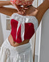 Woman wears red velvet corset with white ruffle trim and bow, holding bouquet over her face.