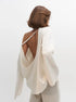 Woman wearing a white open-back knit sweater with a plain background