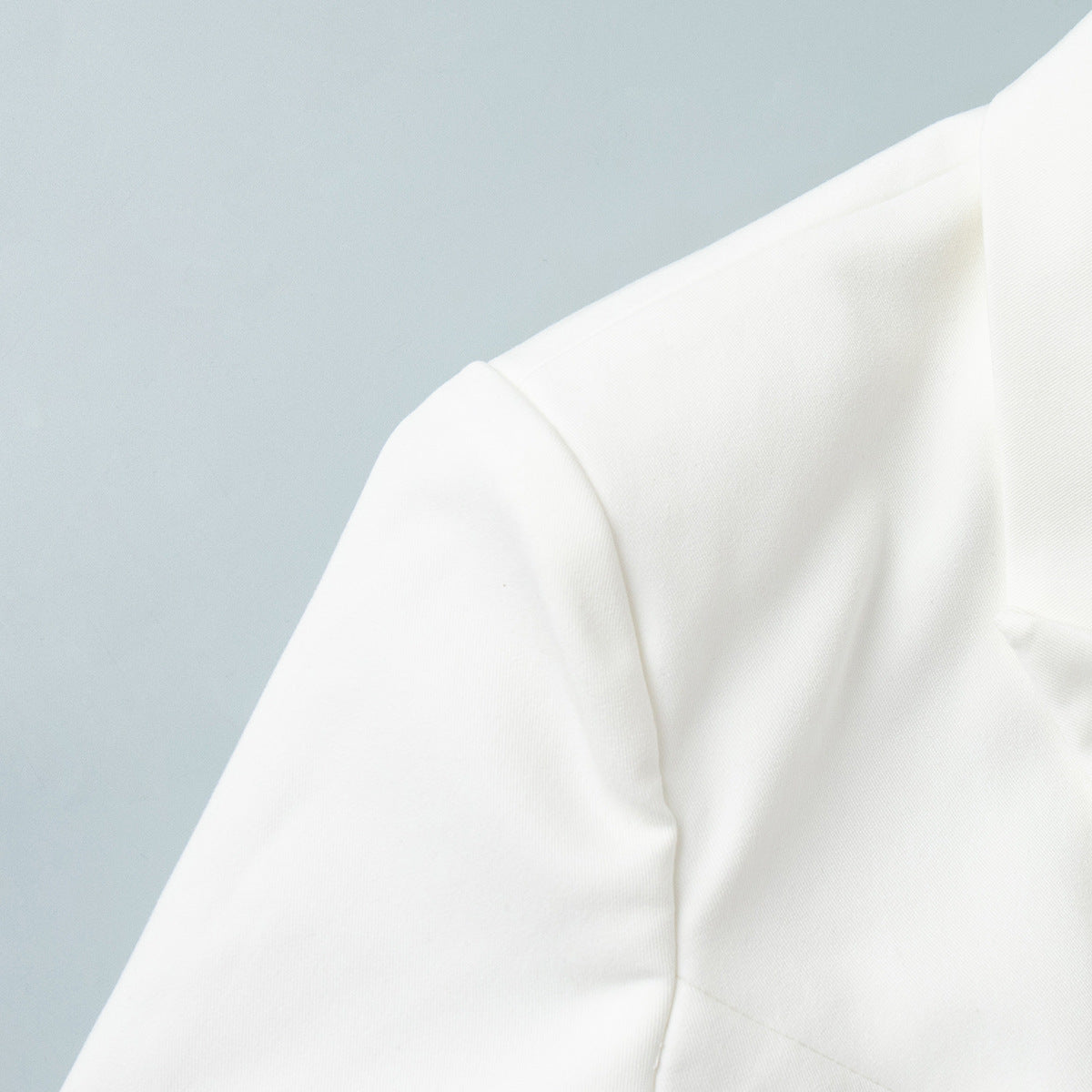 Close-up of shoulder detail of white blazer on a light blue background