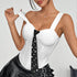 Woman posing in white corset top with thick straps and black pearl-studded tie, styled with pleated leather skirt.