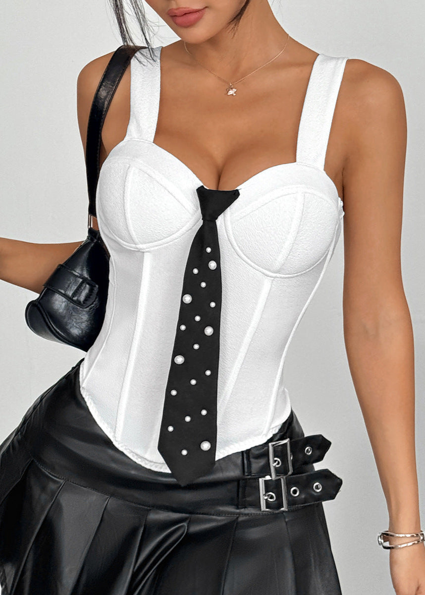 Woman standing in white bustier top with bold seams and black leather skirt, holding black shoulder bag.