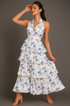 Woman wearing a ruffle white dress with blue floral patterns against a gray background