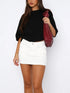 Model wearing a black cropped t-shirt paired with a high waist white denim mini skirt and red woven bag.