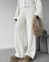 Close view of person wearing a white knit lounge set with a fluffy brown handbag in a minimalistic setting.